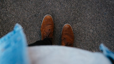 人穿着一双棕色皮靴站在沥青表面
